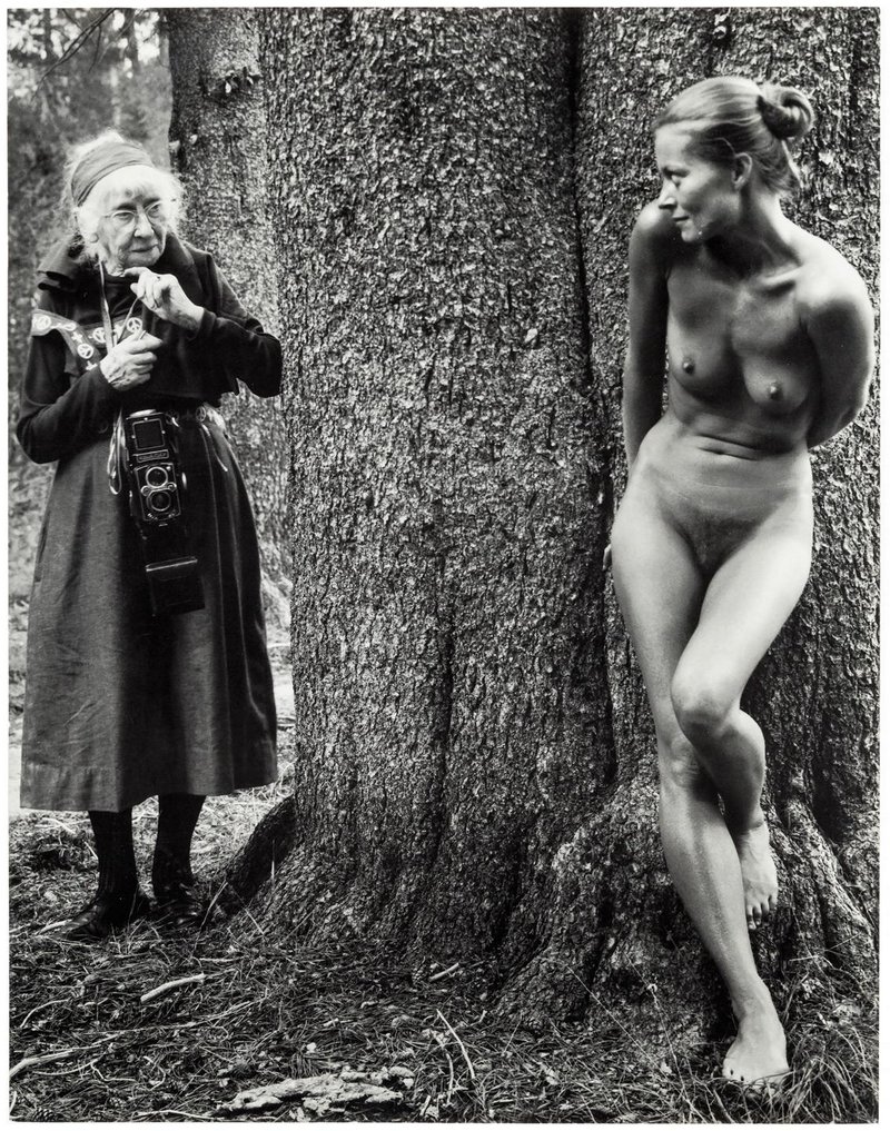 old woman with a camera surprises a lovely and much younger nude model behind a tree as the girl cringes away in shame and tries to hide her pussy