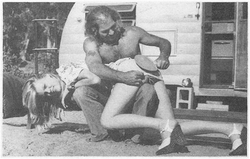 young woman dressed too fancy for a campground is getting an otk paddling from an older redneck man in front of a pull-behind camping trailer