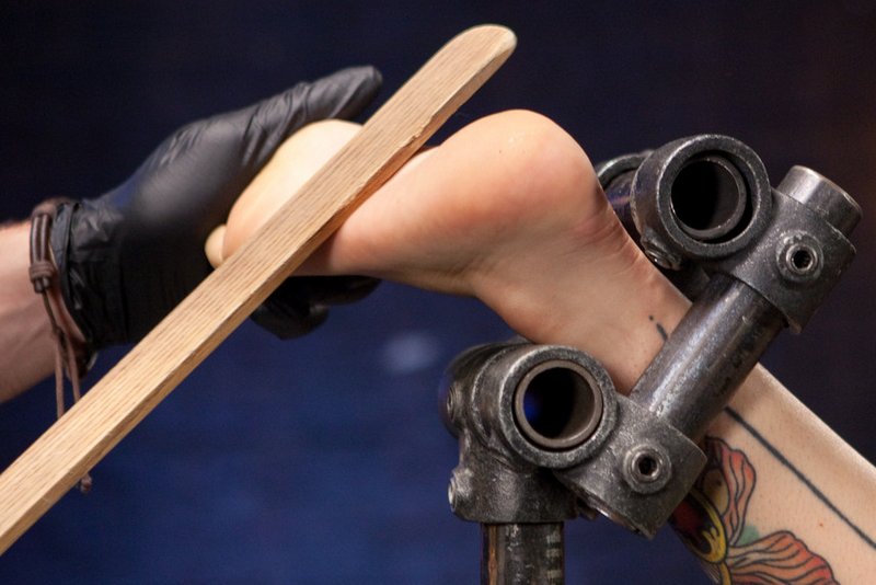 paddling her foot while it's helpless in a steel bondage frame