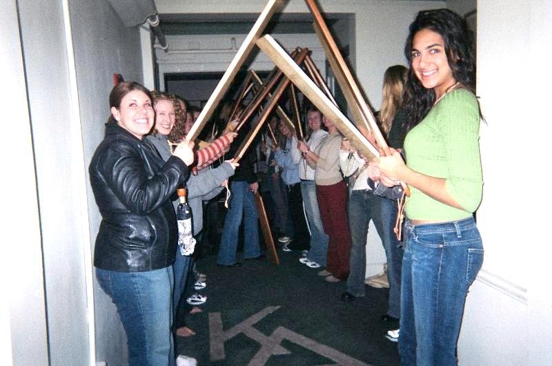 twelve sorority girls line up with paddles in a punishment hallway, all grinning